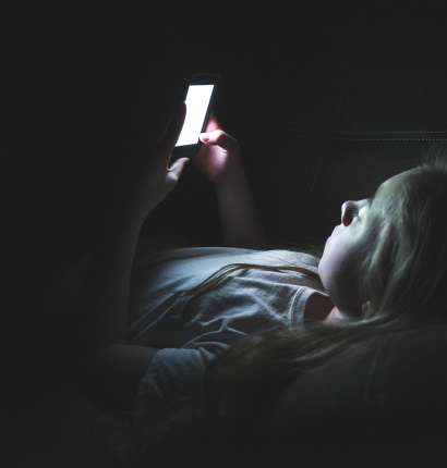 Najstnik v temi gleda v pametni telefon.