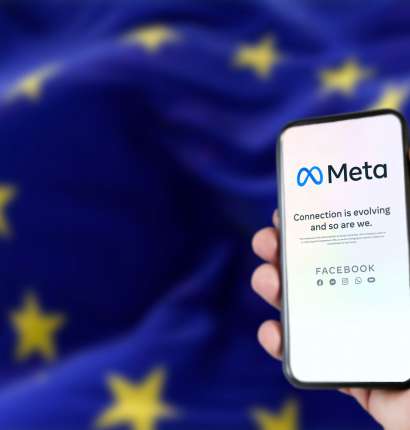 Uporabnik v rokah drži pametni telefon z aplikacijo Meta. V ozadju je zastava EU